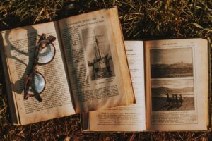 Top view paged of worn out textbooks with pictures and letters placed on grassy ground with eyeglasses in rural area